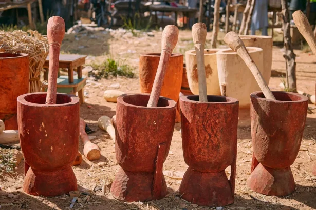 Four wooden mortars with pestles in an outdoor Nigerian market setting under daylight.