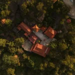 Aerial shot of a temple with red roofs surrounded by dense forest on a hilltop.