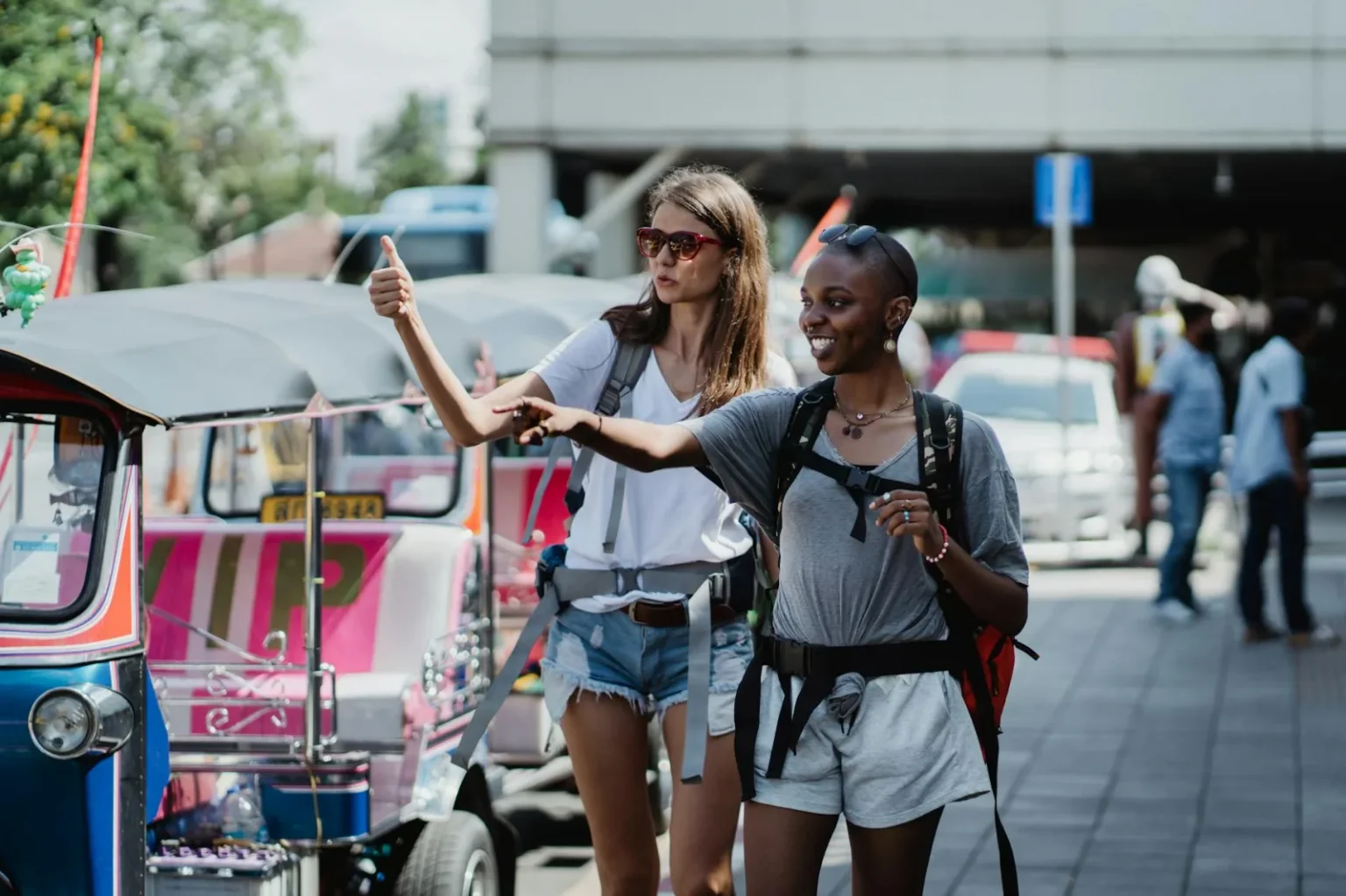 Two tourists with backpacks hailing a tuk-tuk ride in an urban setting, exploring new destinations.