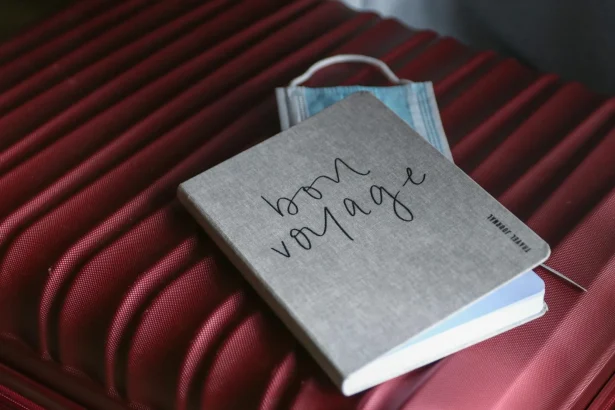 Close-up of a travel journal and mask on a red suitcase, symbolizing preparation for a voyage.
