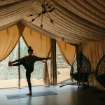 A woman practices yoga in a luxurious glamping tent, surrounded by nature and relaxation.