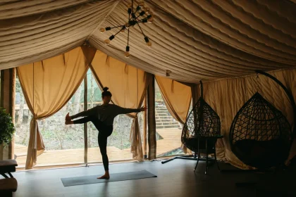 A woman practices yoga in a luxurious glamping tent, surrounded by nature and relaxation.