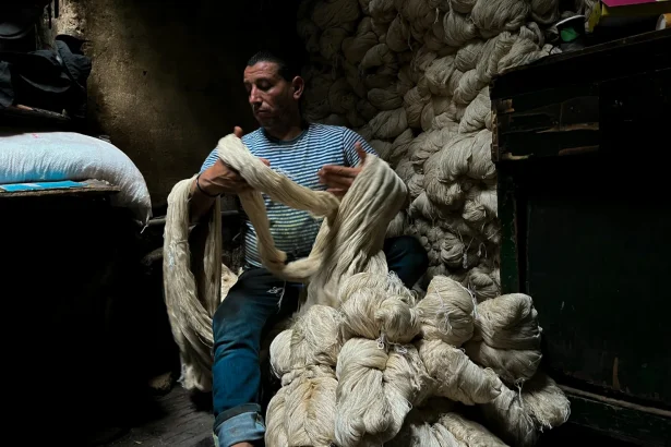 Craftsman handling bundles of natural yarn in a traditional Cairo workshop.