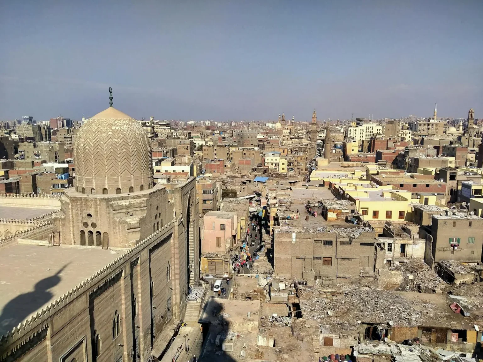 Aerial view of historic Old Cairo showcasing dense residential buildings and a prominent mosque dome under clear skies.