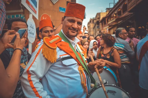 Man in traditional attire playing drums at a lively Cairo street festival.