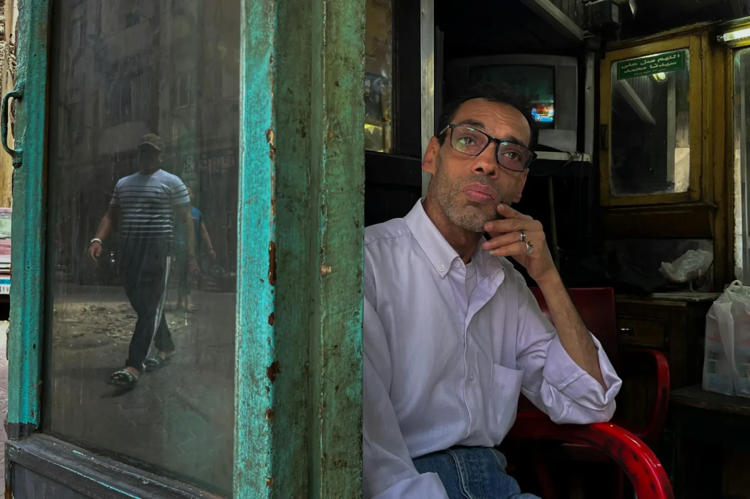 Middle-aged man pondering in a rustic Cairo shop with street reflections.