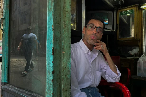Middle-aged man pondering in a rustic Cairo shop with street reflections.