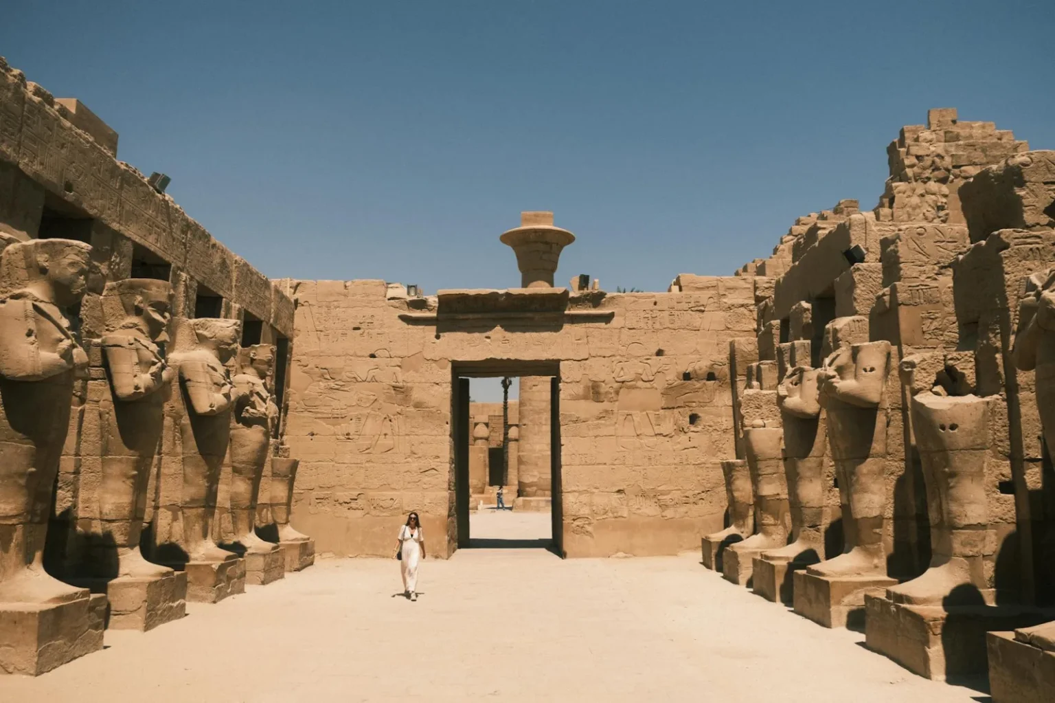 Explore the ancient Karnak Temple in Luxor with grand statues and historical architecture under the summer sun.