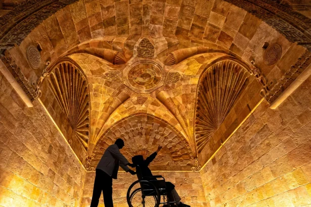 Silhouette of a man assisting a person in a wheelchair under a historic, ornately decorated arched ceiling.
