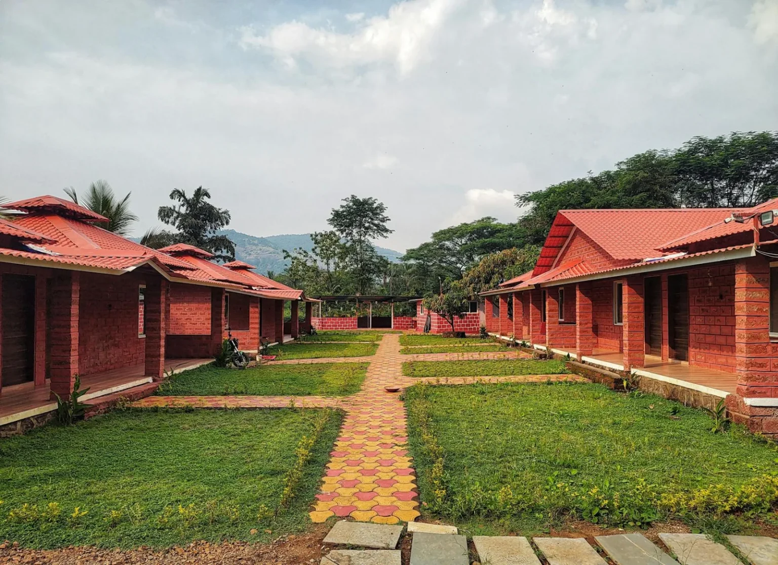 Picturesque red brick bungalows lined along lush gardens with scenic mountain views.