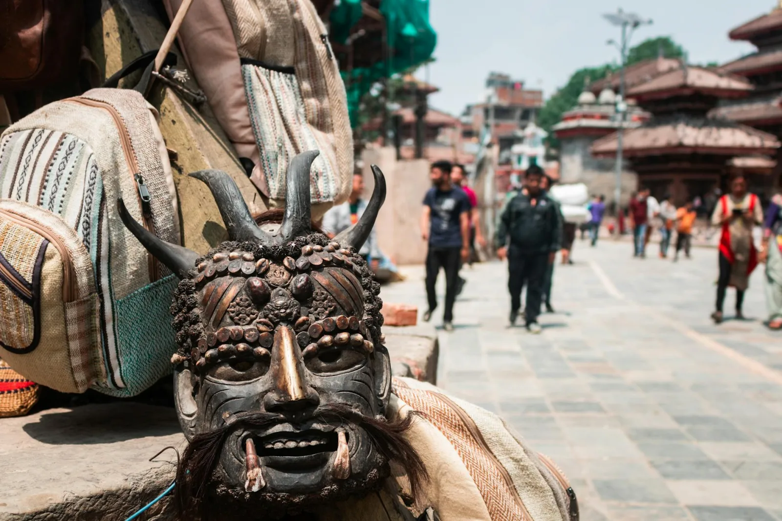 Close-up of a traditional mask and backpacks in Kathmandu's vibrant street market.