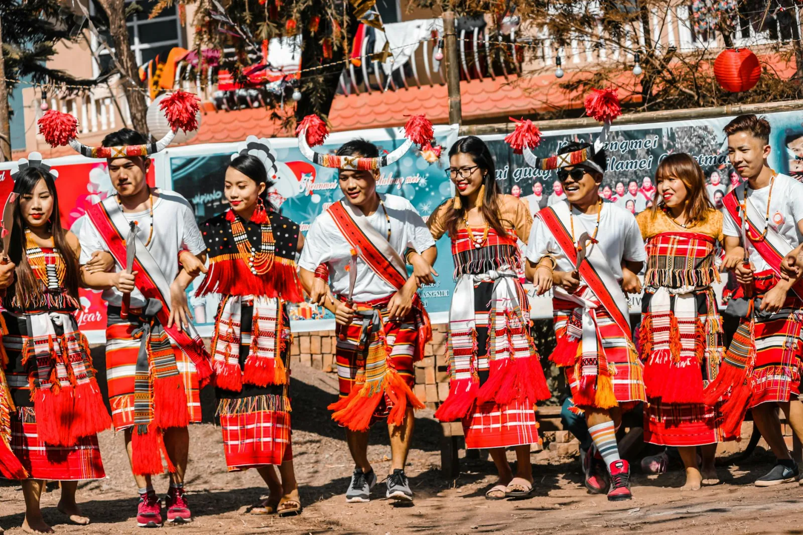 A group of people performing a traditional cultural dance outdoors, wearing tribal costumes.