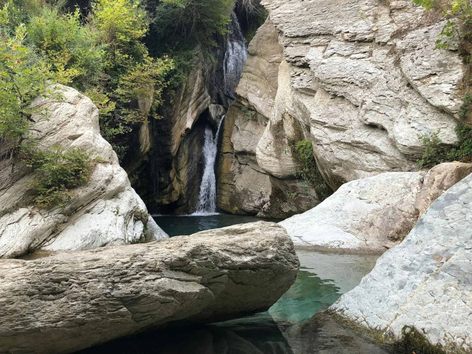 Beautiful waterfall flowing into a clear pool surrounded by rocky cliffs and lush greenery.