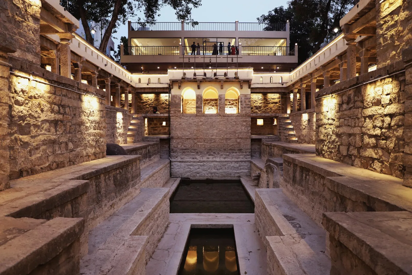 Discover the illuminated Bansilalpet Stepwell in Hyderabad, showcasing intricate stone architecture against the evening sky.