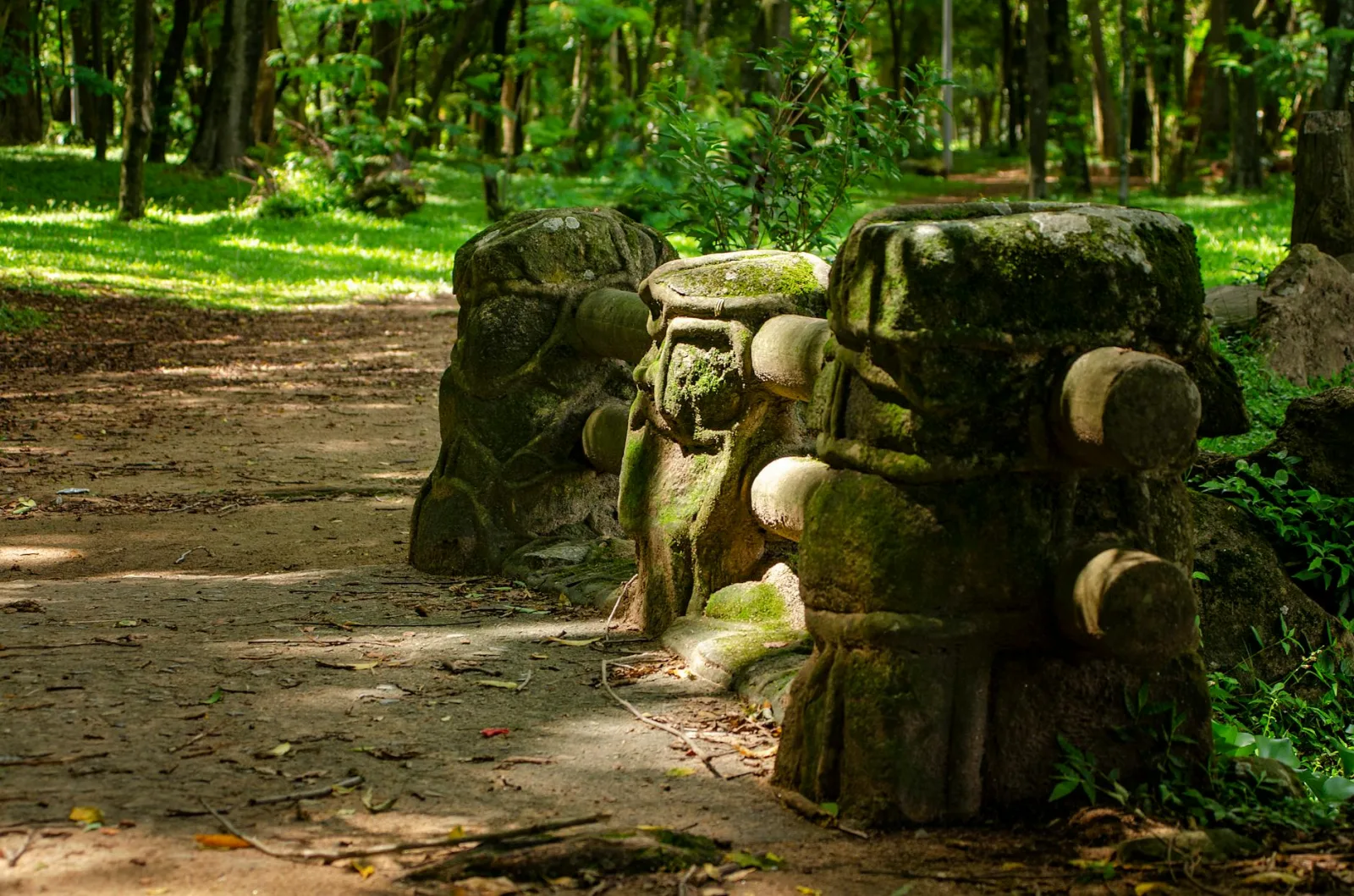 Moss-covered stone sculptures along a forest pathway in a serene park setting.