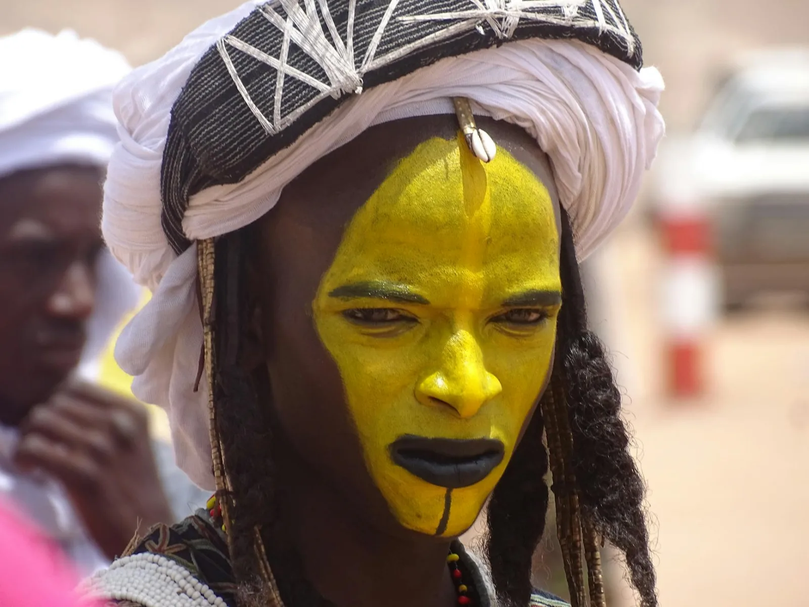 Close-up of a Wodaabe individual with vibrant face paint and traditional attire in Ingall, Niger.