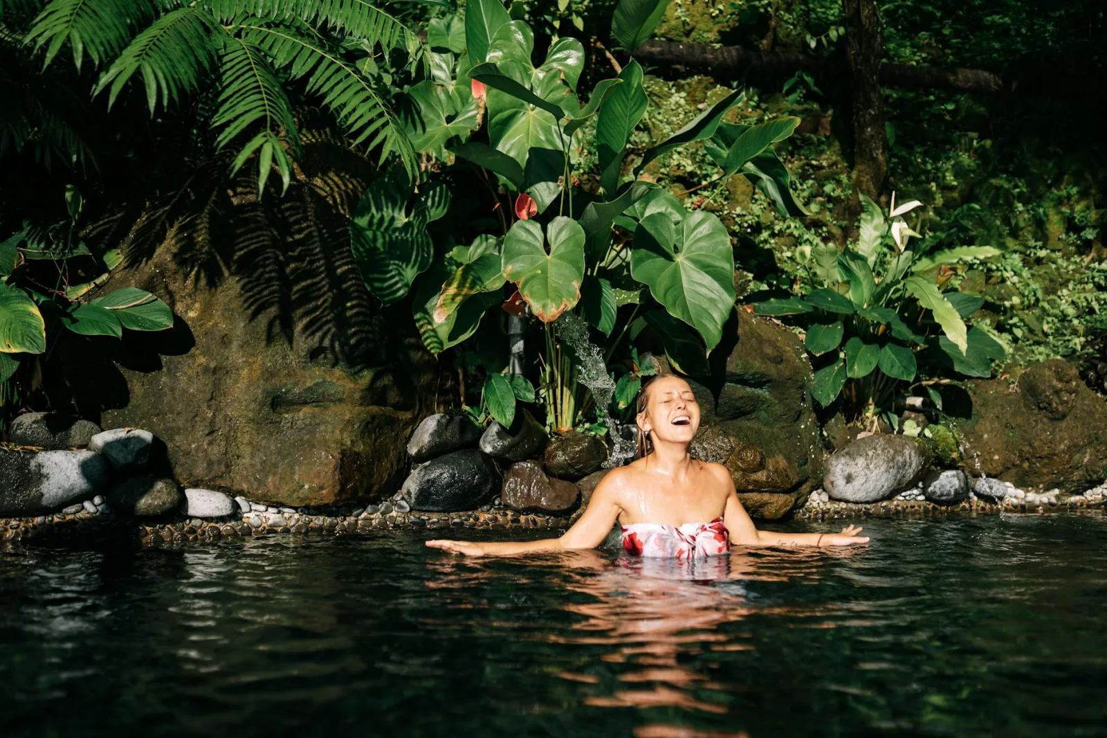 Smiling woman in a tropical jungle pool surrounded by lush greenery.