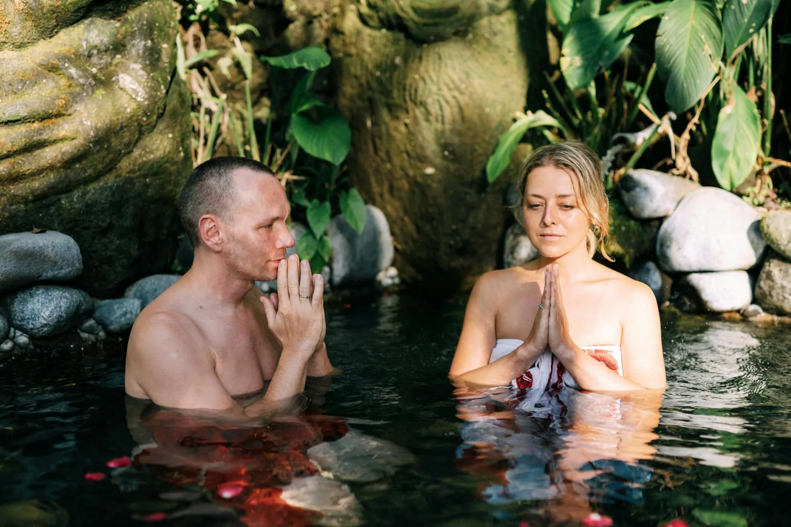 A serene couple meditating in a natural pond surrounded by lush greenery, fostering relaxation.