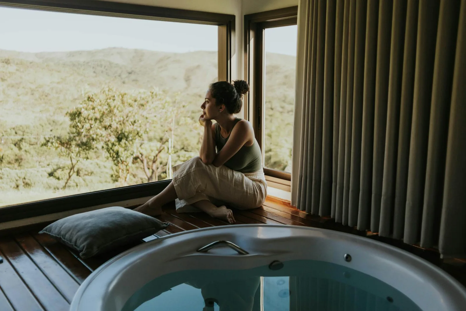 Woman gazing through window beside indoor jacuzzi overlooking mountains.
