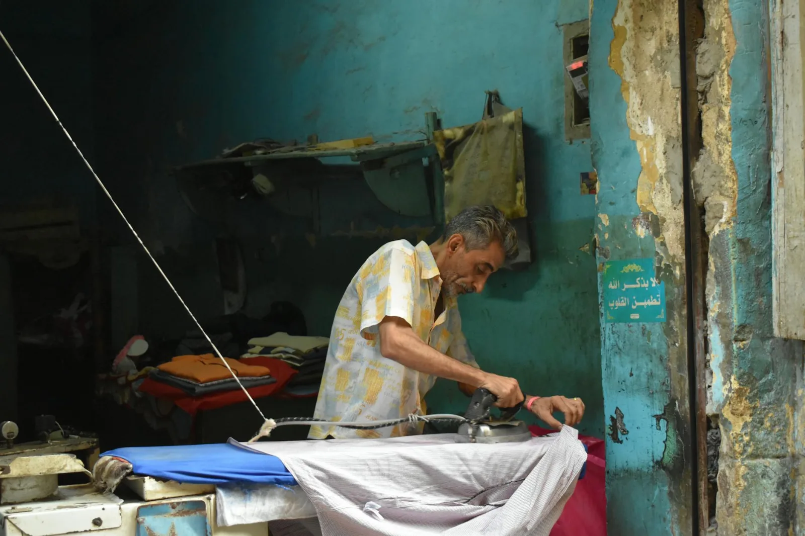 An adult man ironing clothes in a rustic street corner shop in Cairo, Egypt.