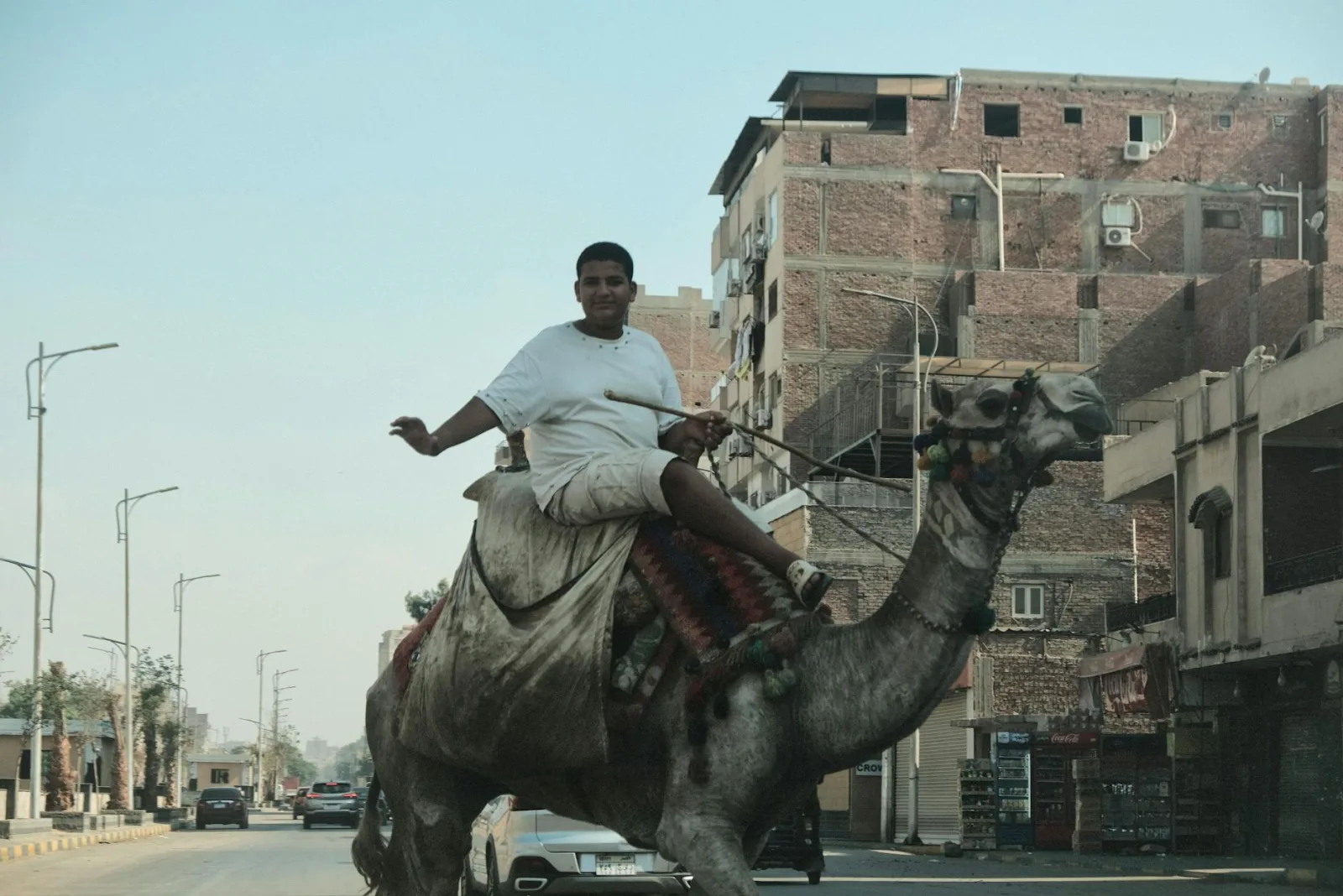 A young man rides a camel through the streets of Cairo, showcasing traditional and modern life coexistence.