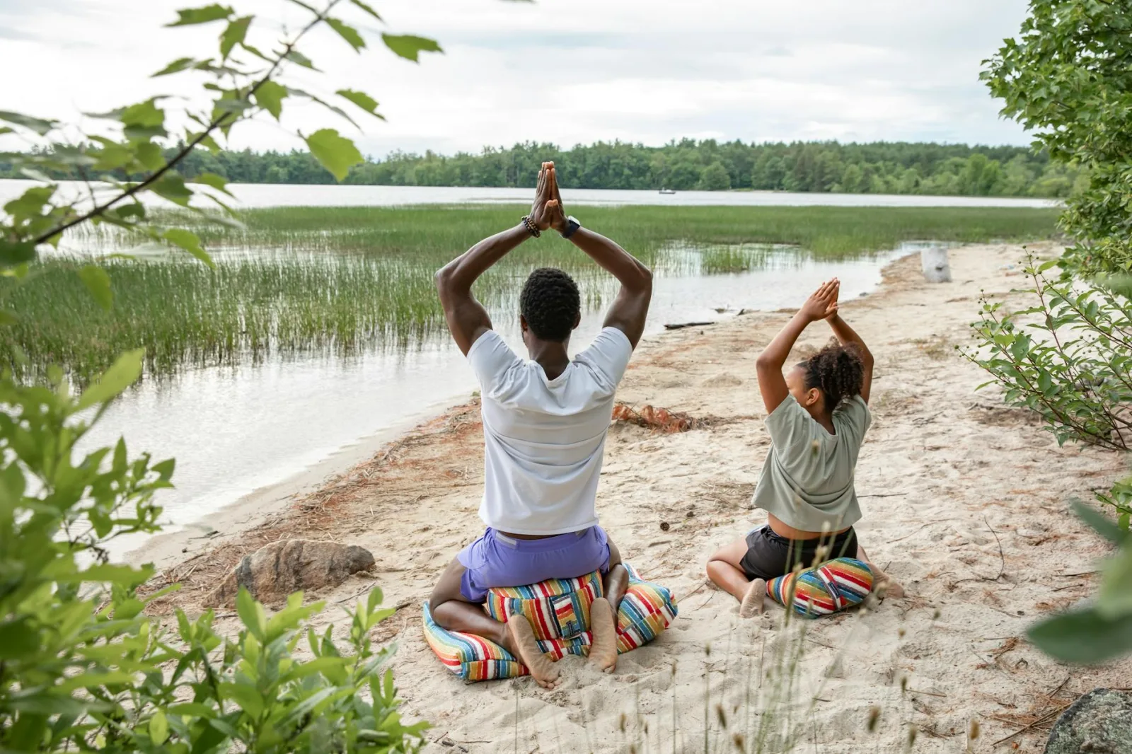 Two people practice yoga peacefully by a serene lake in New Hampshire, surrounded by nature.