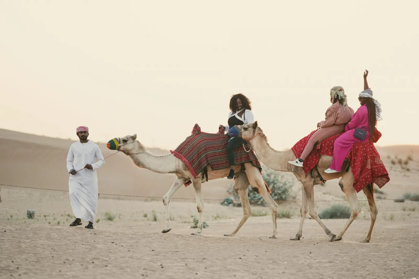 Women enjoying a camel ride adventure in the scenic Dubai desert at sunset.