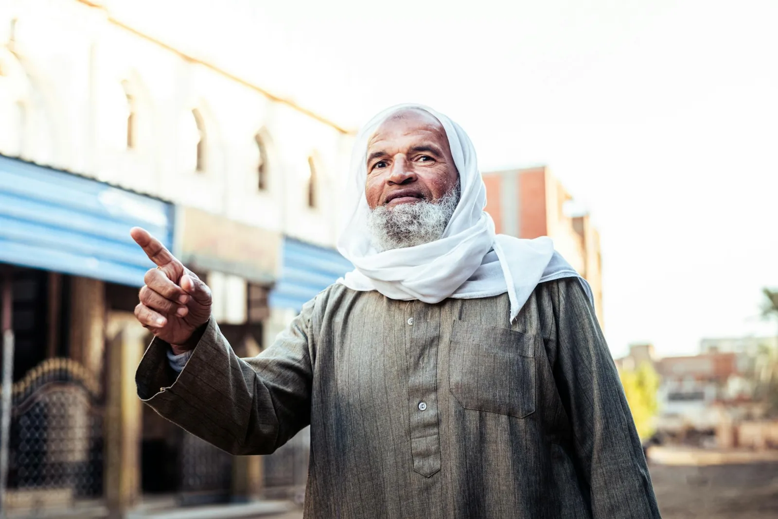 Elderly man in traditional Egyptian attire gestures outdoors, capturing cultural essence.