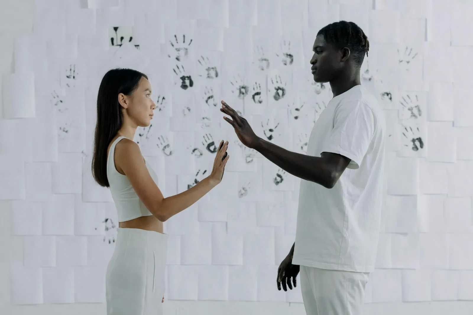 A man and woman standing face to face in front of a wall covered with handprints, exploring themes of connection and diversity.