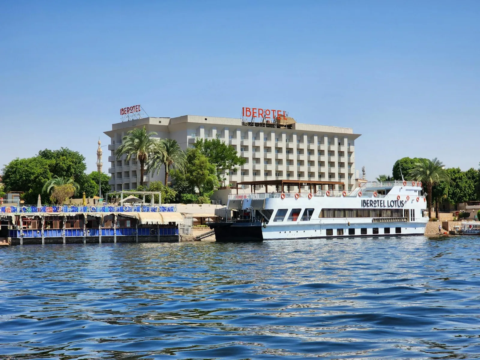 Scenic view of Hotel Iberotel by the Nile River with a cruise boat docked nearby.