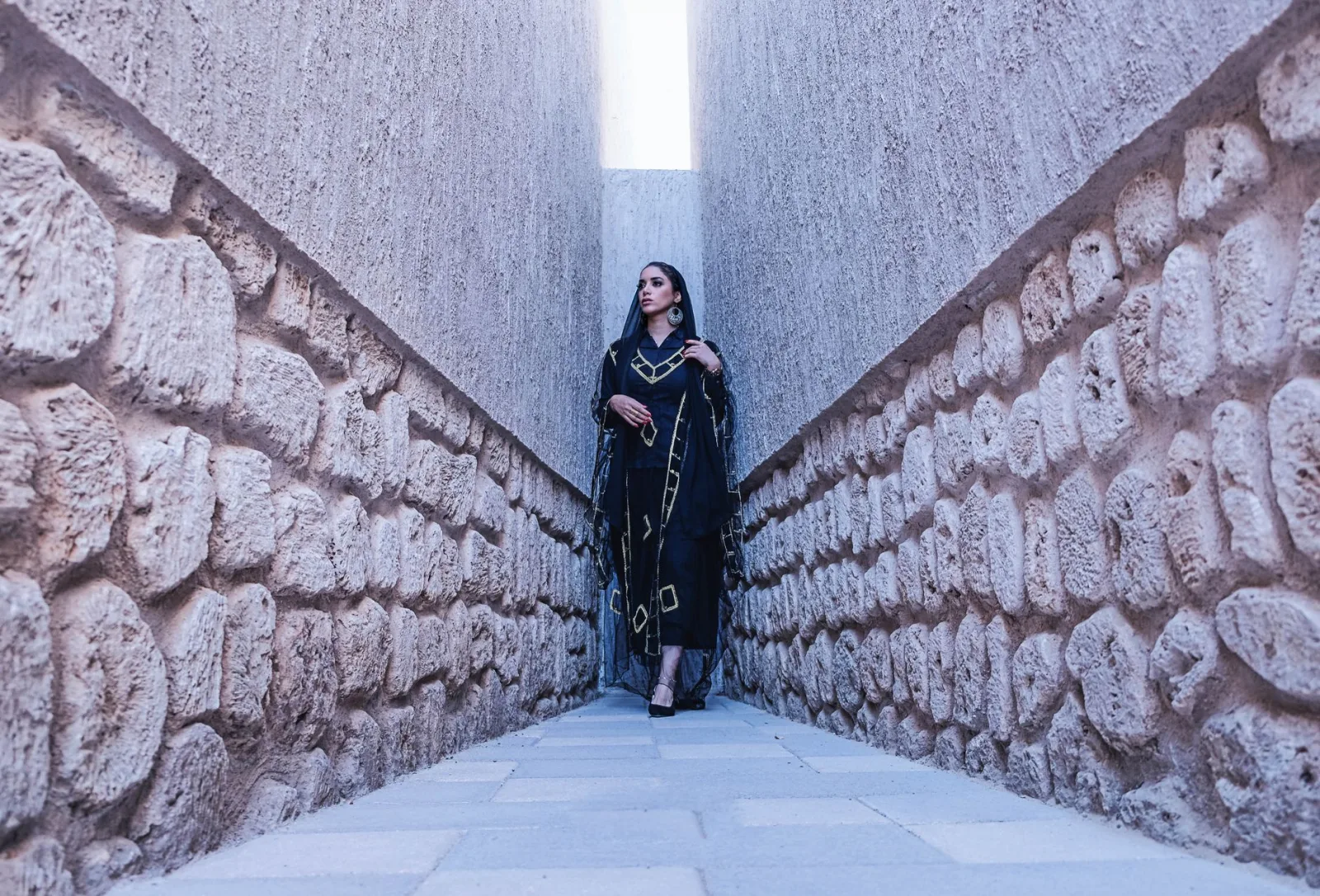 A woman in traditional attire walking through a stone alley in Dubai, showcasing Middle Eastern architecture.