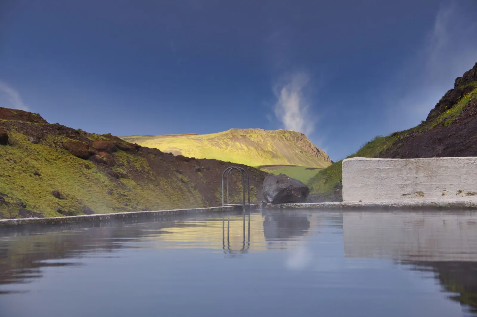 Relaxing hot spring pool in the scenic Icelandic mountains with clear blue skies.