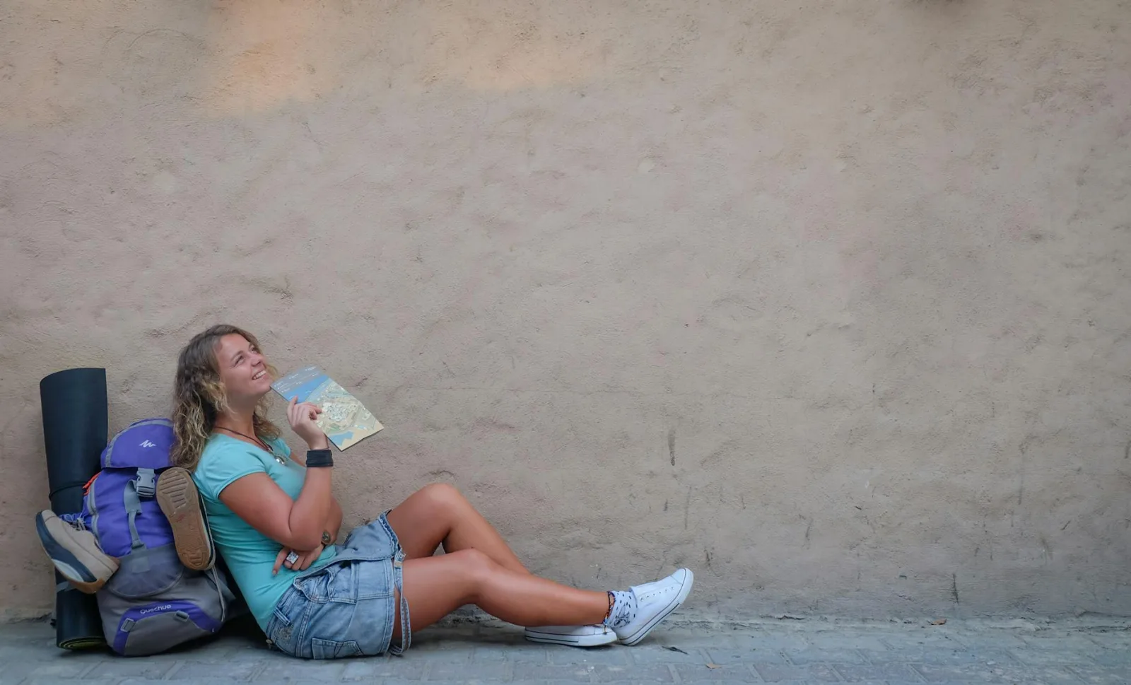 Smiling female traveler sitting by a wall with a map, enjoying a moment of relaxation on her journey.