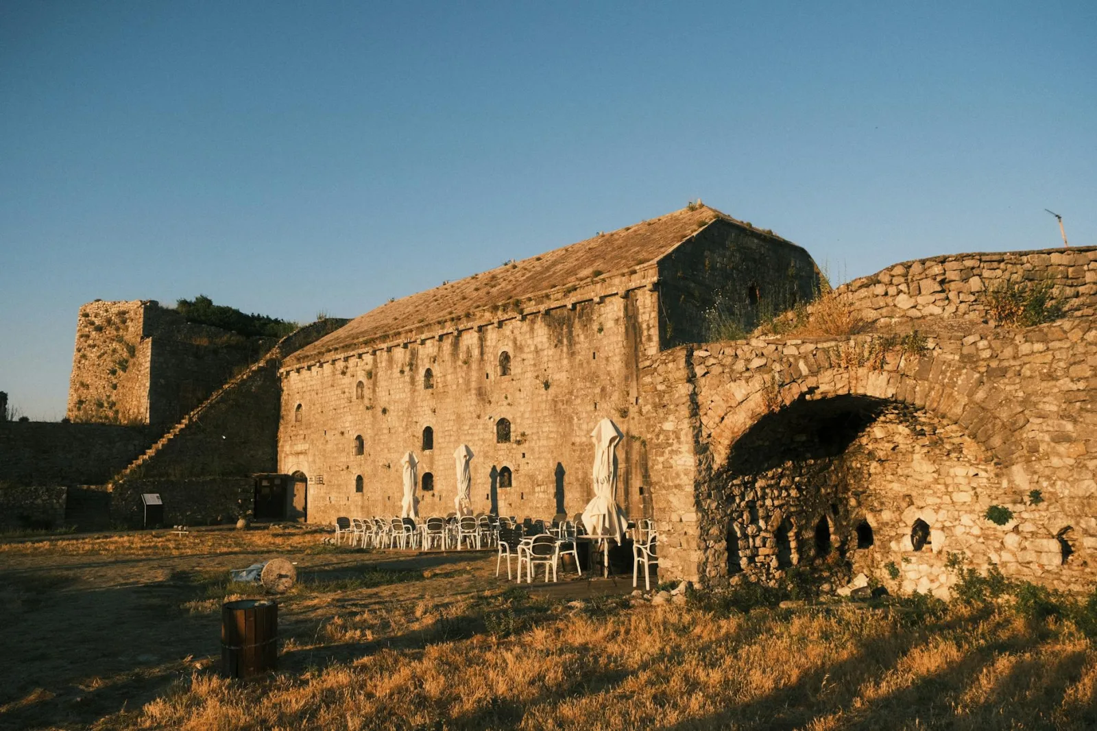 Historic Shkodër Castle in Albania at sunset with empty outdoor seating.