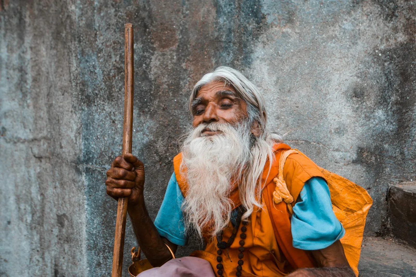 Portrait of an elderly man with a white beard and walking stick, outdoors.
