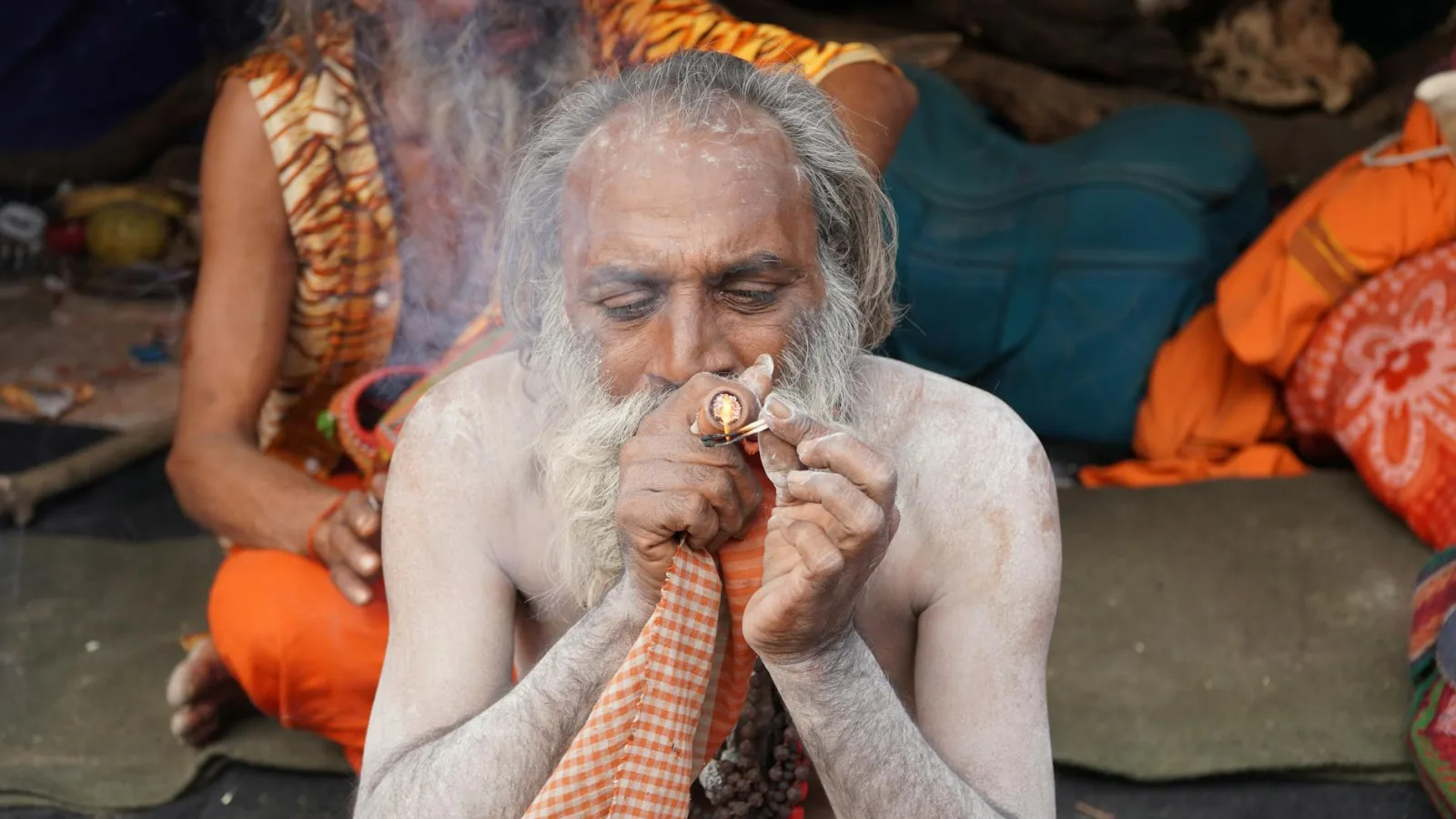Elderly sage performing a smoking ritual with intricate pipe amid spiritual decorations.