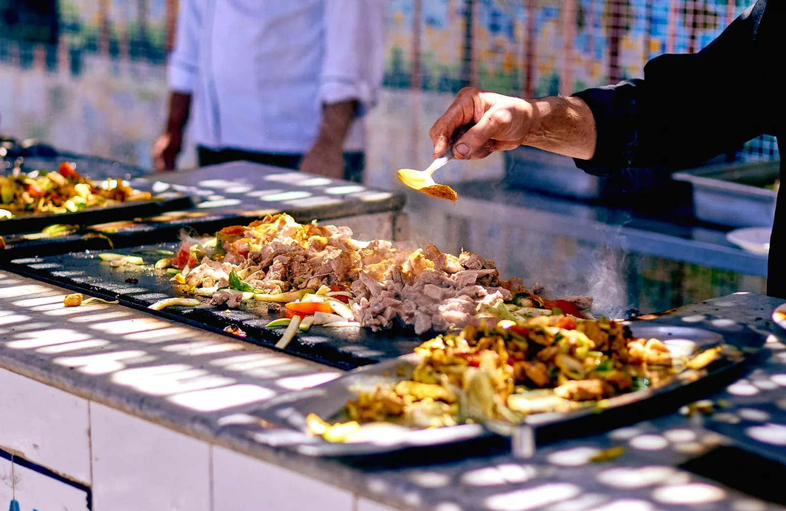 Chef adds spices to sizzling meat and vegetables at a vibrant street food stall.