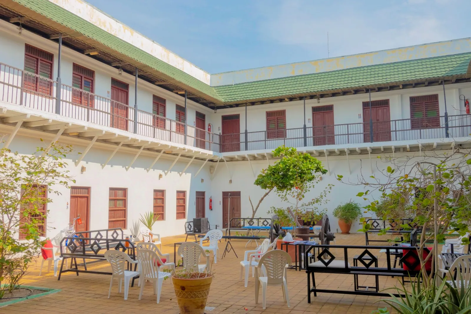 Bright courtyard with seating, surrounded by green-roofed architecture and lush plants.