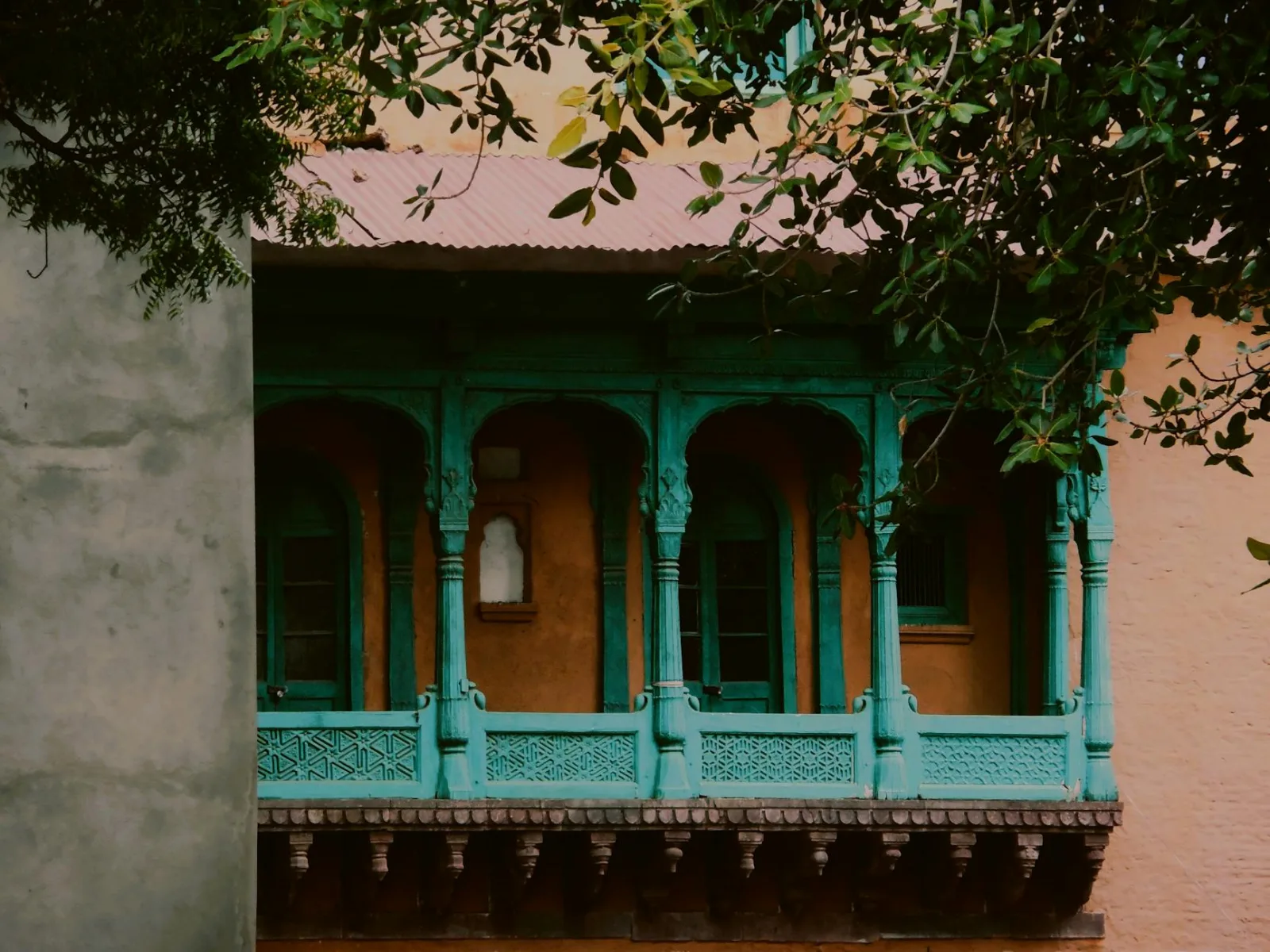 Charming vintage balcony with intricate turquoise wooden designs surrounded by lush greenery.