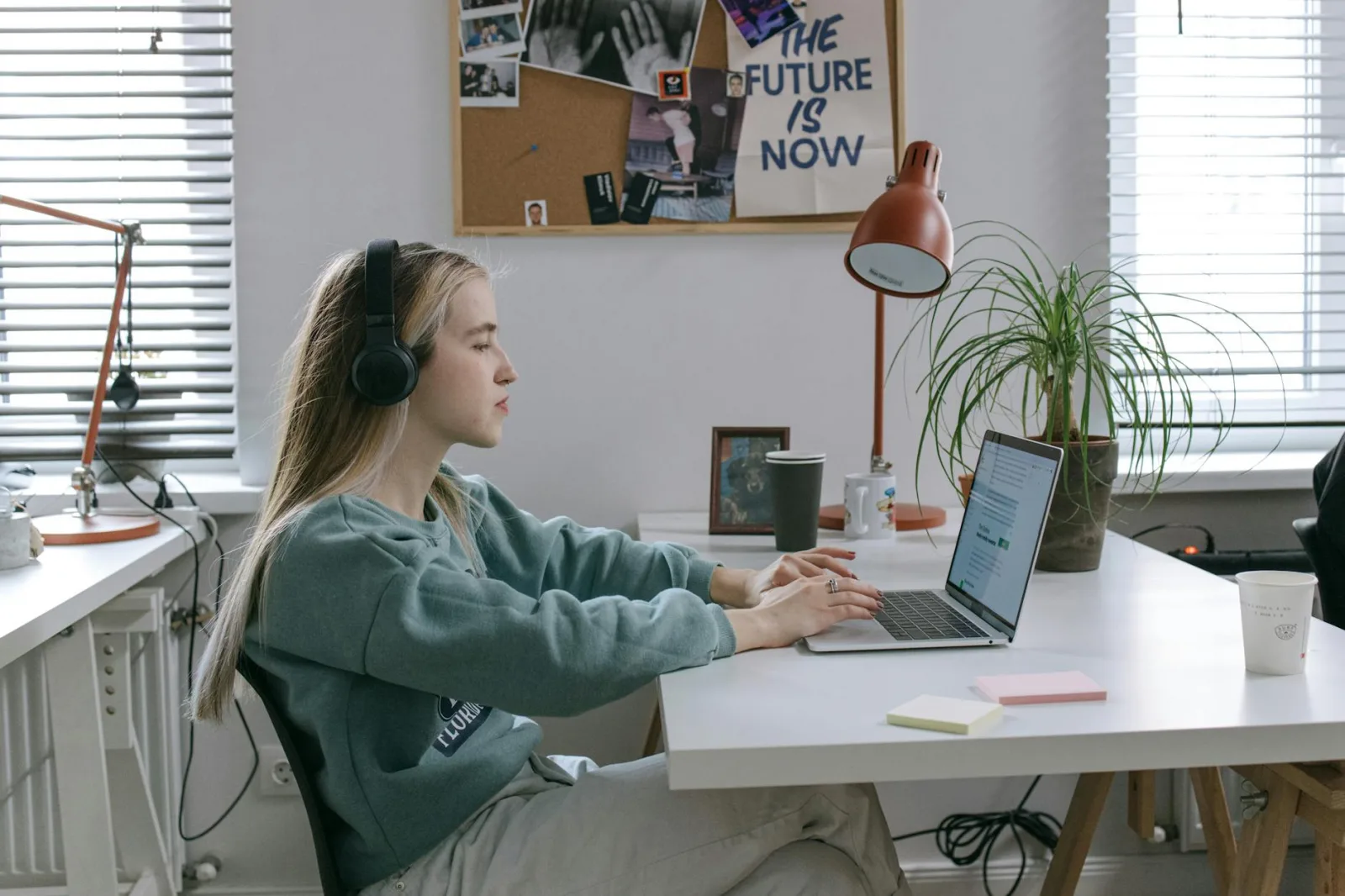 Focused young woman with headphones working on a laptop in a modern office setup.