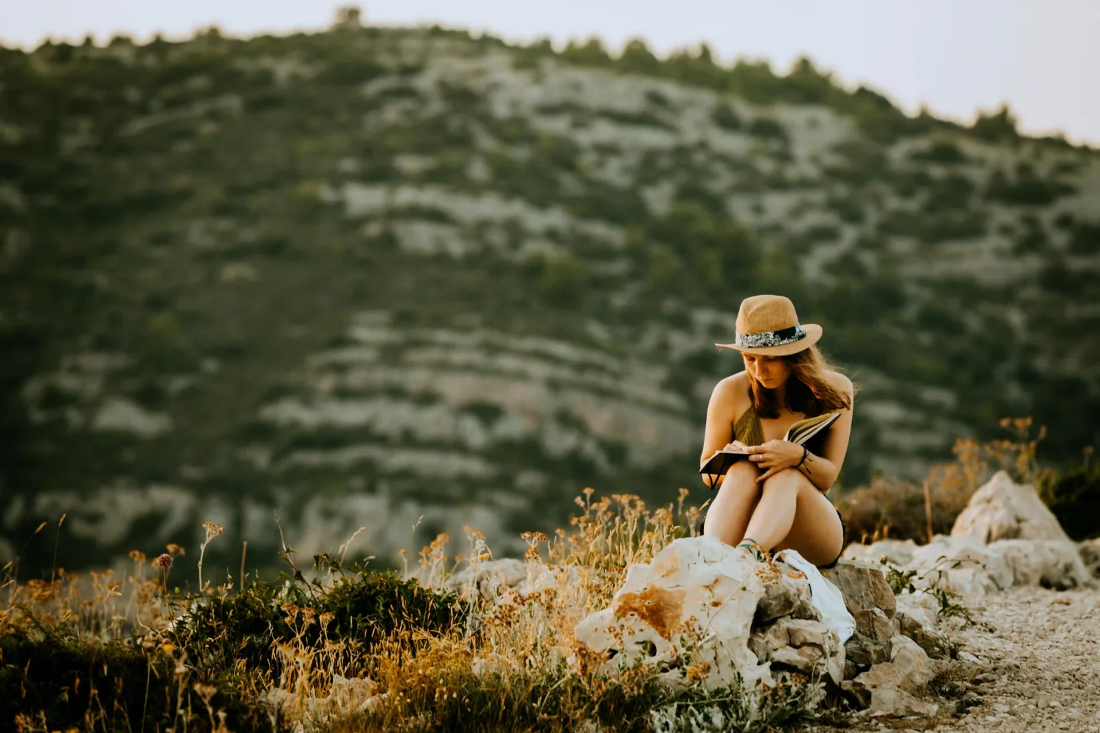 Woman enjoys a peaceful reading moment in a scenic mountain setting, epitomizing summer leisure.