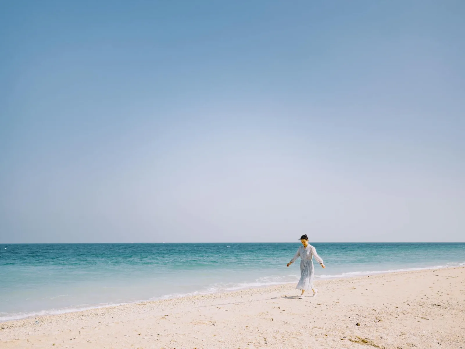 A serene beach scene with a person walking along the sand in Beihai, China under a clear blue sky.