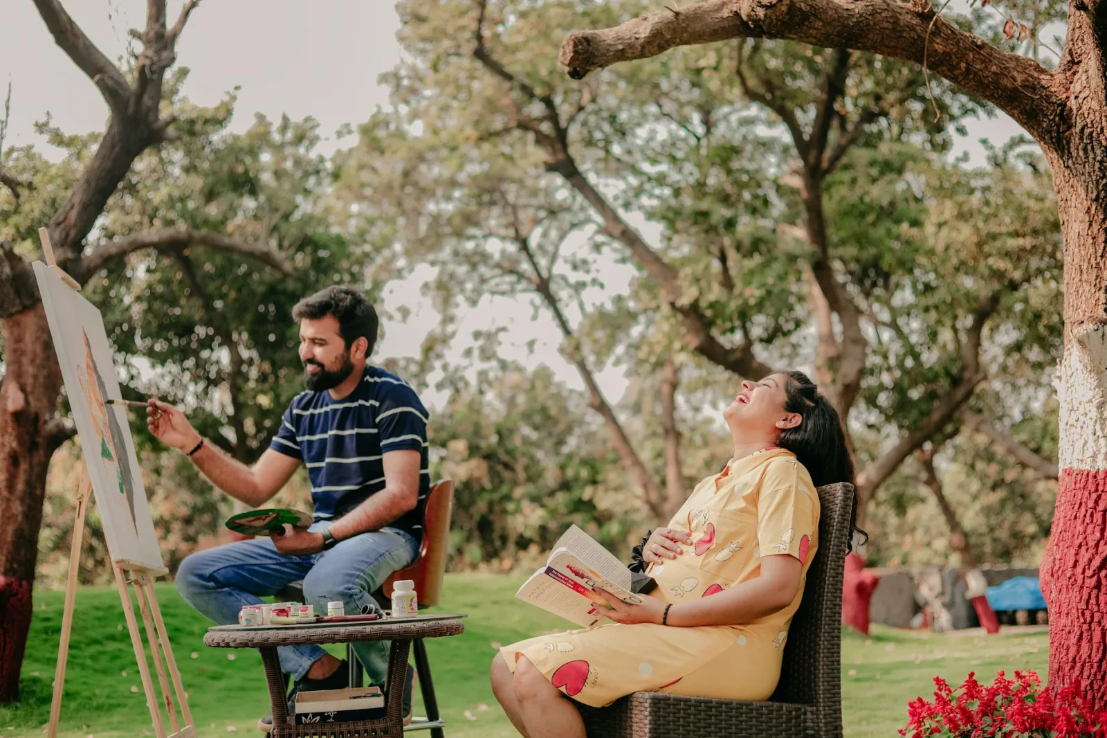 Couple relaxing outdoors with painting and book, capturing a joyful moment under a tree.