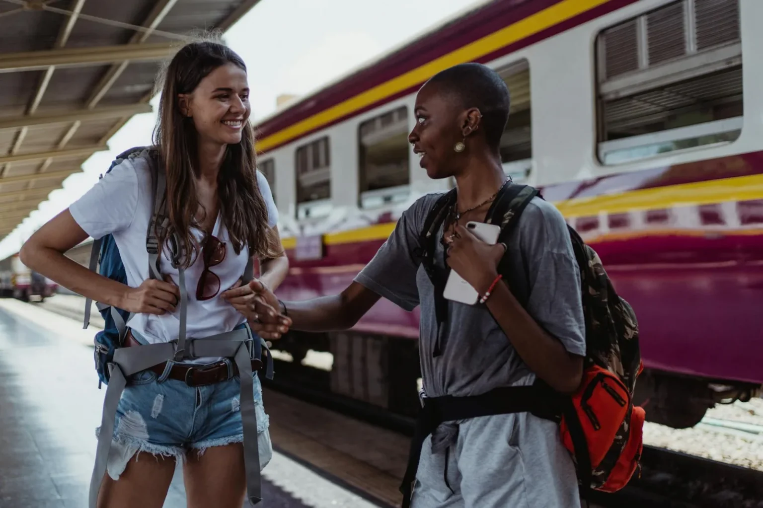Two women smiling and talking while waiting at a vibrant train station.