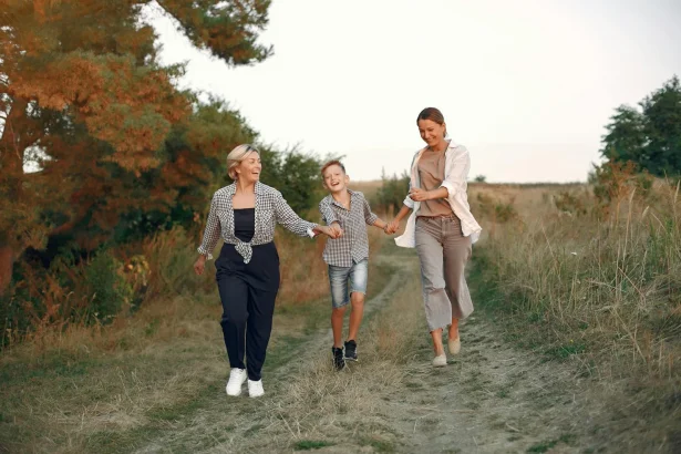 Full body delighted adult mother and preteen son strolling together with middle age grandmother hand in hand on path in summer field during weekend in nature