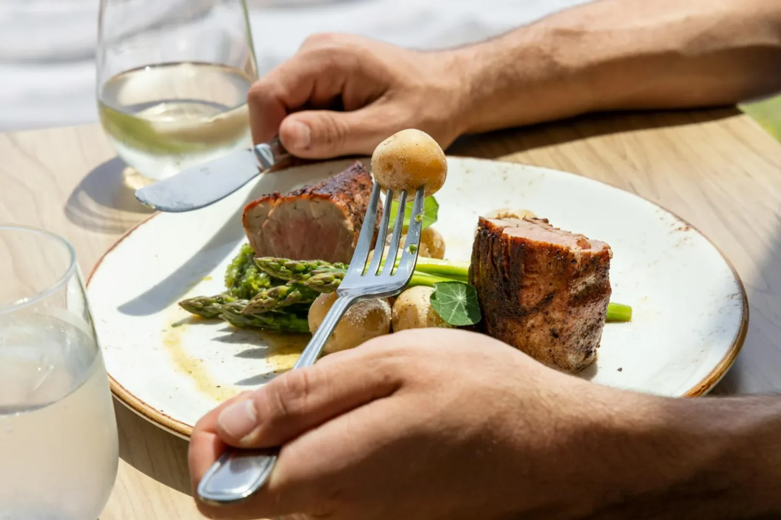 Close-up of a gourmet meal featuring pork, asparagus, and potatoes on a sunny day.