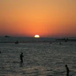 A stunning sunset at Yanbu beach with silhouettes of people enjoying the water.