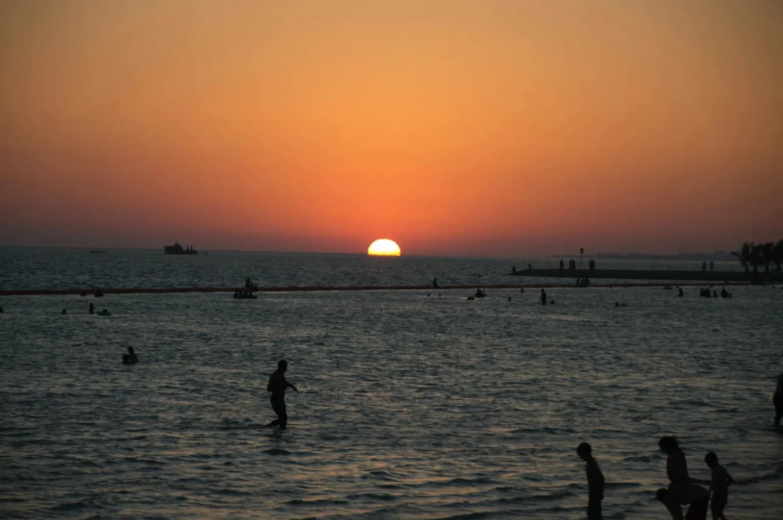 A stunning sunset at Yanbu beach with silhouettes of people enjoying the water.