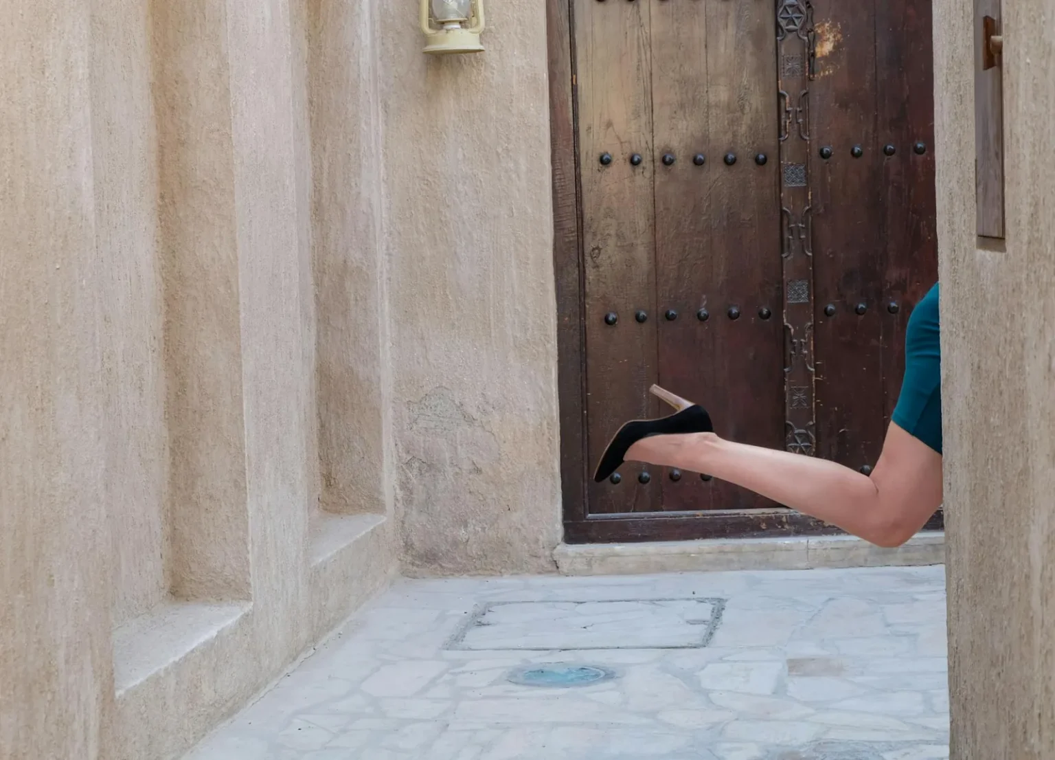 A woman's leg in heels playfully extends from a corner near a rustic wooden door in Dubai.