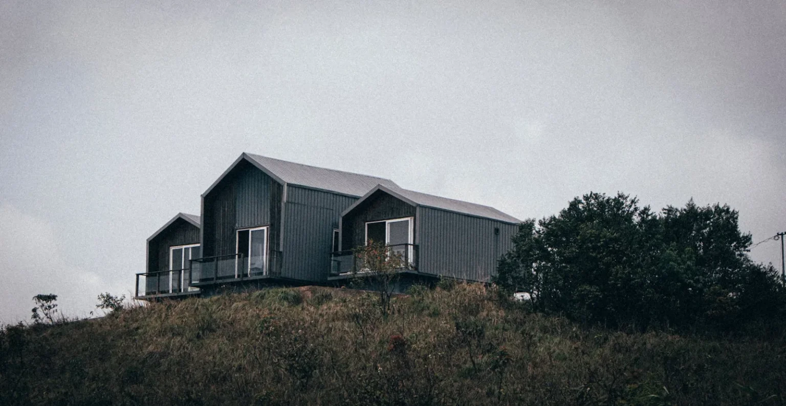 Contemporary cabin perched on a hillside in a cloudy, rural setting.
